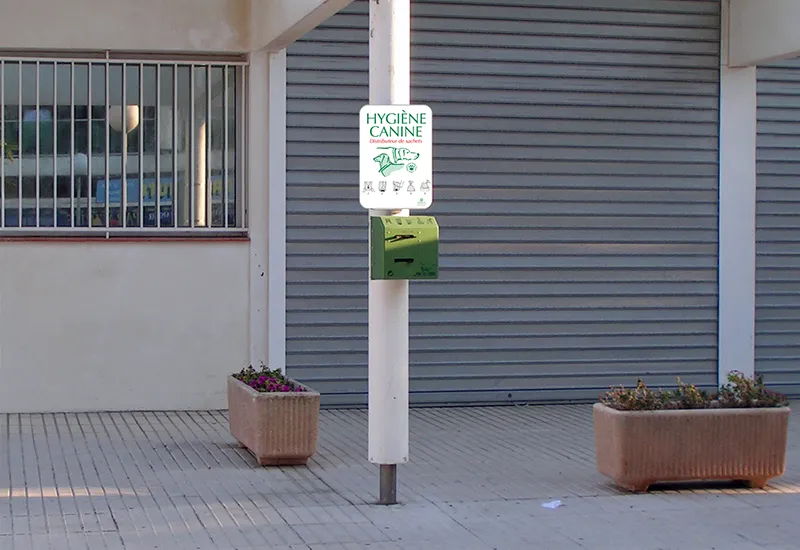 Distributeur canin double rouleaux avec affichage Distributeur canin double rouleaux sur poteau avec affiche de sensibilisation d'hygiène canine dans une rue.