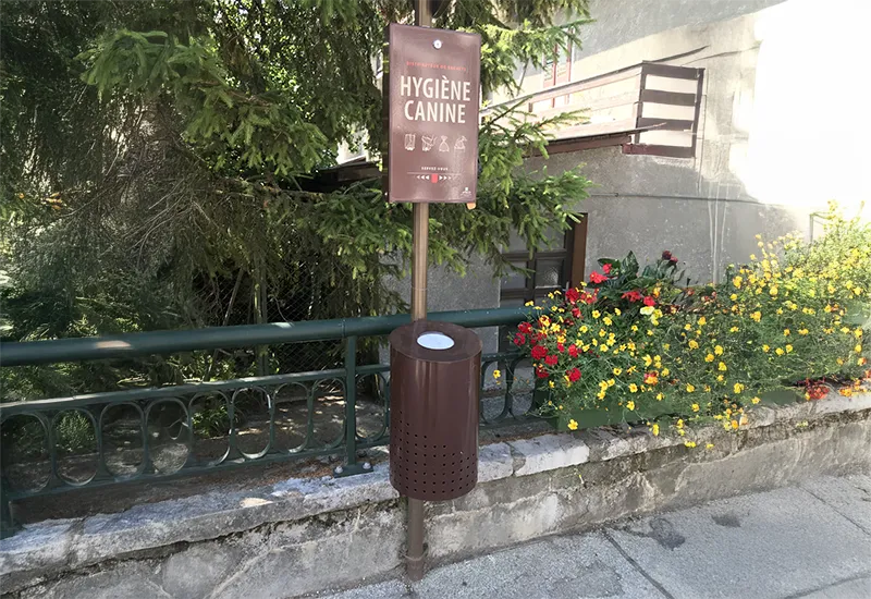 Duo distributeur canin et poubelle à clapet Duo distributeur canin et poubelle à clapet marron sur mât sur un trottoir.