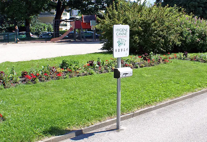 Duo distributeur canin en rouleau avec panneau de sensibilisation Duo de distributeurs canins et panneau de sensibilisation dans un parc.