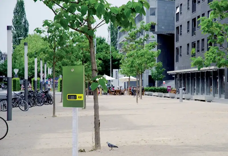 Distributeur canin à liasse vert Distributeur canins vert practica belloo sur pied près d'un arbre dans une ville.